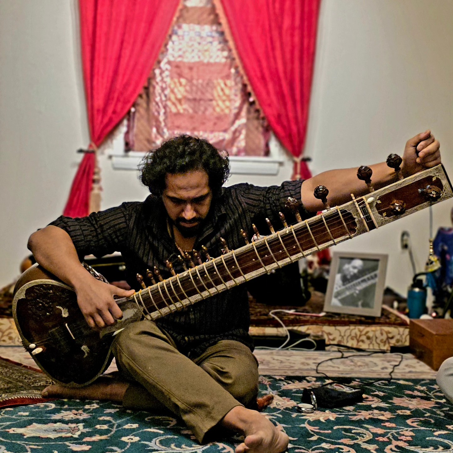 Playing sitar indoors with red curtains
